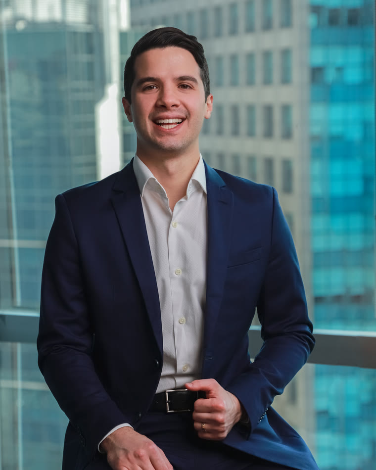Dr. Danilo Mardegam Razente de terno azul-marinho, sorrindo, com prédios de São Paulo ao fundo